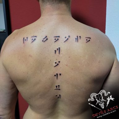Drachenschrift Schriftzug Rücken-Tattoo Rücken-Tattoo mit vertikalem Schriftzug in Drachenschrift, mittig entlang der Wirbelsäule.