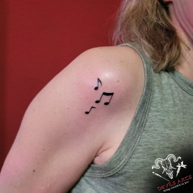 Kleines Musiknoten-Tattoo auf der Schulter mit feinen schwarzen Linien.