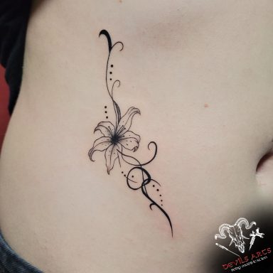Blumen-Ornament Tattoo an der Leiste mit feinen Linien und dekorativen Punkten.