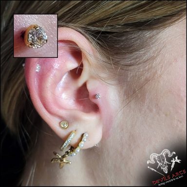 Tragus-Piercing mit goldenem Kristall-Stecker am Ohr.