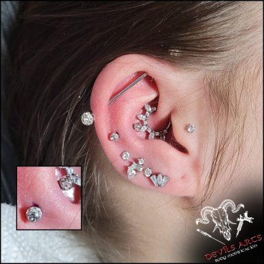Snug-Piercing mit silbernen Kugeln und umlaufendem Kristallring am Ohr.