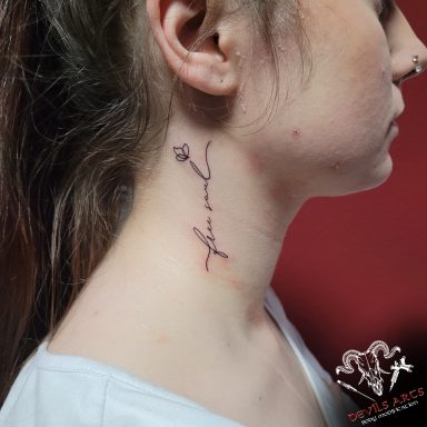 Fineline Schriftzug-Tattoo „free soul“ mit kleiner Blume am Hals.